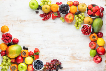 Rainbow fruits background, strawberries raspberries oranges plums apples kiwis grapes blueberries mango persimmon on white wooden table, top view, copy space for text, selective focus - obrazy, fototapety, plakaty