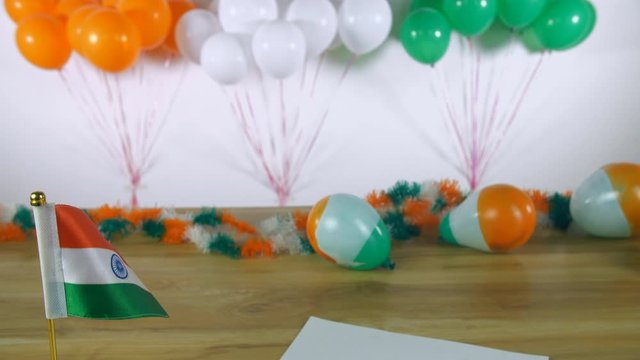 Tilt shot of woman hands writing 'Happy Republic Day' text on a festive card. Beautiful festival decorations like tricolor balloons  ribbons  Indian national flag for Republic day/26 January celebr...
