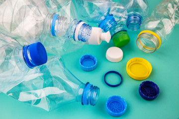 Crushed plastic bottles and colorful caps on vivid cyan blue background.