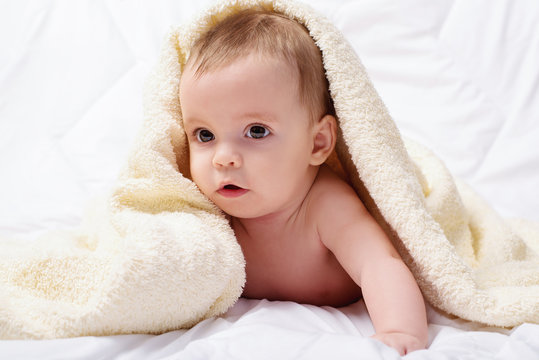 Laughing baby wrapped in the towel on bed 