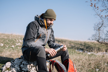 Bearded hiker resting on a stone and holding thermos
