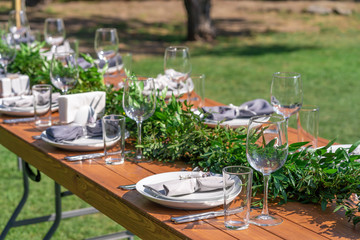 Beautifully decorated wooden table in a summer open-air cafe. Green branch and fresh flowers table decoration