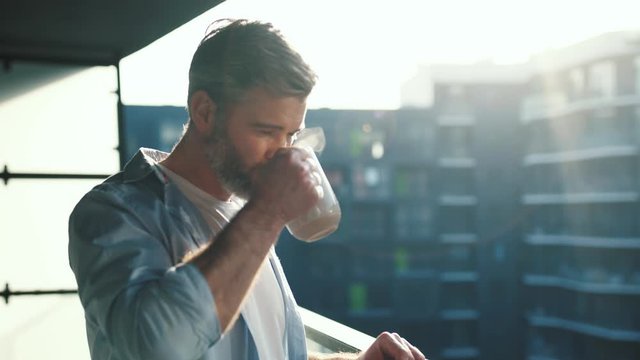 Close up view of caucasian middle aged manwith grey hair in balcony with great views drinks hot coffee or tea, sun shine, enjoying beautiful morning feeling happy