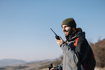 Smiling man speaking on two-way radio for hiking - obrazy, fototapety, plakaty