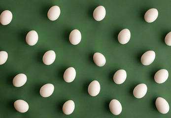 Flat lay of white naural organic eco hen eggs organized on dark olive green background in pattern