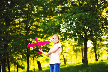 Little girl launches a toy plane into the air in the park outdoor. Child launches a toy plane. Beautiful little girl stands on the grass and launches a pink toy plane.