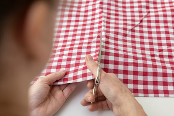 La costurera corta la tela con unas tijeras, vista desde atrás