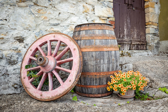 an old wagon wheel, a wooden barrel and a pot with flowers