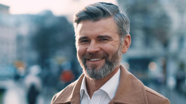 Extrime close up view of attractive middle aged man looks to the camera and smile in city center street success business outdoor portrait serious elegant feel happy great morning slow motion