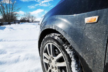 Close-up of a car on the snow near the road with trees against blue sky with clouds