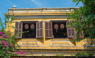 Typical view of Hoi An ancient town streets. The second floor of the cafe building. Open wooden shutters on the windows. Birdcages hang in the window opening.