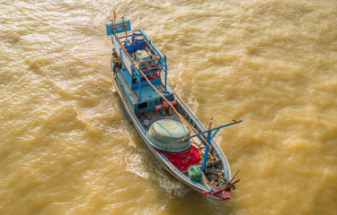 A small fishing boat is sailing in the sea for fishing. The photo was taken from above and from the side. Brown sea water due to the recent typhoon and many river sediments.