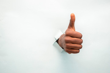 black hand doing a thumbs up through a hole in a cardboard paper