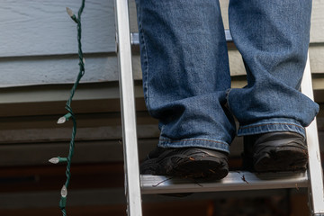 mans black shoes standing on silver ladder with christmas lights