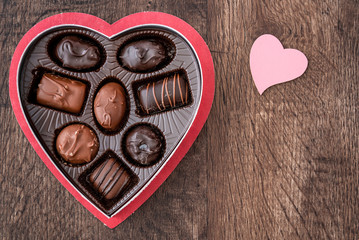 Simple heart shaped box of chocolate Valentine’s Day candy on a wood table, with a pink wood heart