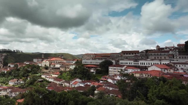 Motion time lapse of fast moving clouds against a blue sky passing above the colonial mining city Ouro Preto in Minas Gerais, Brazil, with sun rays lighting up parts of the city through clearances
