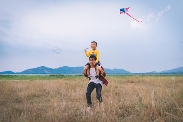 Happy family Father and child with a kite and bubble amid of nature in the summer on wide meadow..