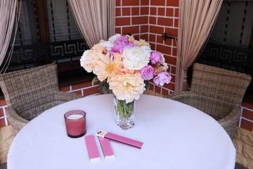 Bouquet of flowers with pink and yellow peonies on a white table with wicker furniture
