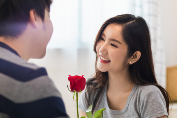 Fototapeta na wymiar Asian lovely couple man and woman in bedroom together. Boyfriend give rose to girlfriend in romantic moment of love. Warm heart marriage bonding and relationship. Lover anniversary Valentine concept..