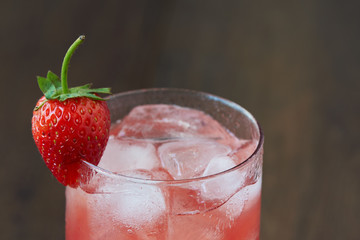 A glass of tasty cold strawberry juice with ice on the table.