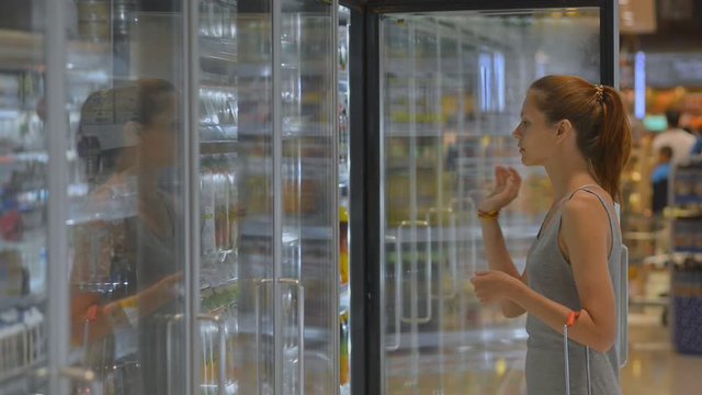 Young woman shopping in supermarket opening fridge to take refrigerated food drink. healthy organic juice in bottle. shopping, buyer, cooler concept. customer buying grocery at store