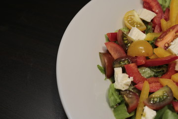 Salad of vegetables in a white plate close-up on a dark background