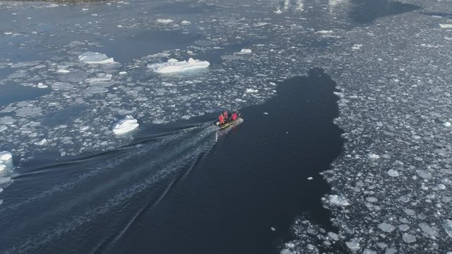 Zodiac motor boat sailing in Antarctic ice. Aerial tracking shot - drone flight overview of south pole ocean landscape. Rubber boat float in winter open water brash ice. Footage shot in 4K (UHD)