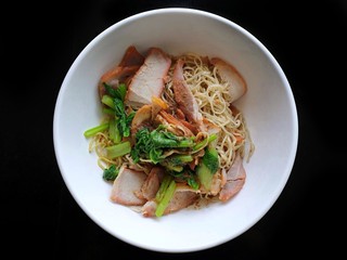 Top view of egg noodle with bbq pork, shrimp wonton topped with sliced scallion in white bowl isolated on black background, Chinese food style, Ready to eat or serve