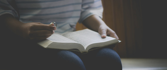 Christian girl holding a ring and reading Bible book inside a church.