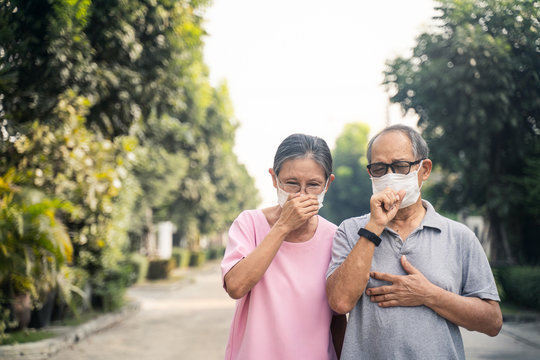 Asian Elder Senior Couple Wearing Mask For Prevent Dusk Pm 2.5 Bad Air Pollution. Old Woman And Man Holding Mask And Having A Cough Due To Bad Smell And Allergic Sickness Symptom Stand On Street.