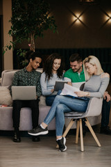 Diverse group of smiling young designer working together over a laptop during a meeting in the boardroom of a modern office