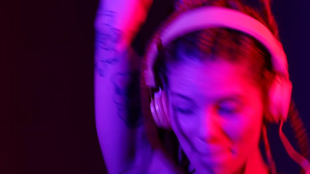 Footage of Dj woman with tree braids, dancing with headphones. With blue and red color lights. The video can be united with my other dj woman footages. Woman Makes different figures 