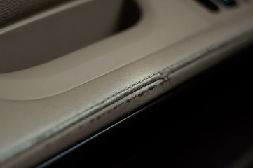 The armrest of the driver's door of the car sheathed in beige leather. Shabby leather interior.