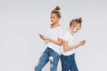 Blonde mom and daughter in white t-shirts and jeans using mobile phones gadgets concept isolated on white background