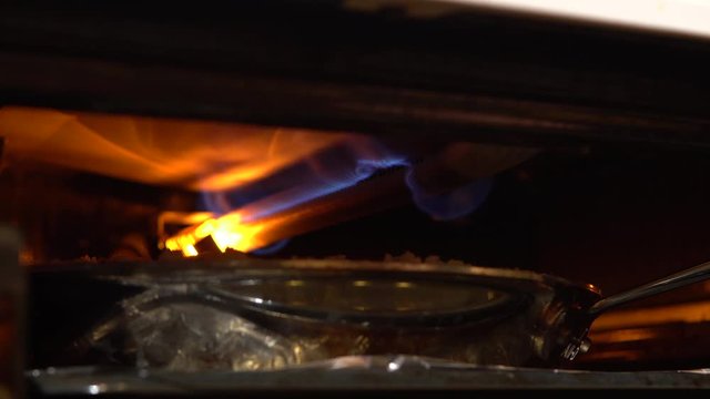 Fire burning inside an oven broiler over a large stainless steel pan - Close up
