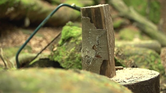 Slow motion close up shot of a axt / hatchet cutting / smashing a log of wood / billet of wood with a saw in the background