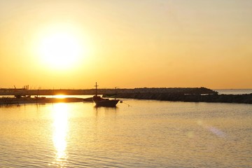 Fototapeta premium The sun rises in the morning along the coast, with boats mooring around the dam preventing coastal erosion.