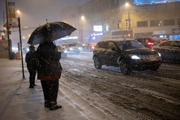 man is standing outside with umbrella in the extreme cold and snow in Chicago area during a blizzard during a winter night in January.  traffic is slowing down due to weather conditions
