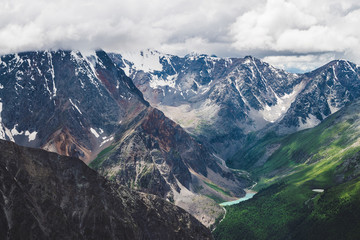 Atmospheric alpine landscape with massive hanging glacier on giant rocks and valley with mountain lakes. Big glacier tongue. Low clouds over snowbound mountains. Majestic scenery on high altitude.