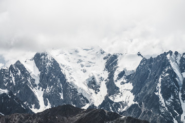 Fototapeta na wymiar Atmospheric minimalist alpine landscape with massive hanging glacier on big mountain under cloudy sky. Cracks on ice. Low clouds over snowbound huge mountain range. Majestic scenery on high altitude.