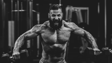 Fototapeta na wymiar Muscular athletic bodybuilder working hard in gym on dark background, dramatic black and white image