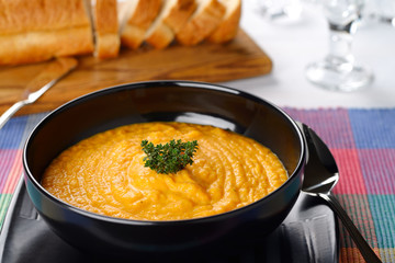 Cream carrot tomato orange soup with thyme garnish in black bowl with sliced bread and glasses
