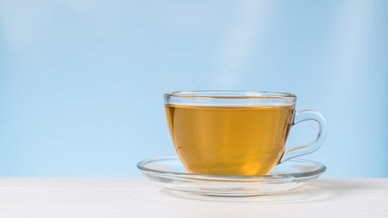 Tea in a glass Cup and saucer on a white table on a blue background.