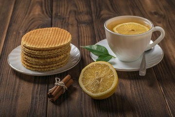 Homemade waffles and tea with cinnamon and lemon on a wooden table.