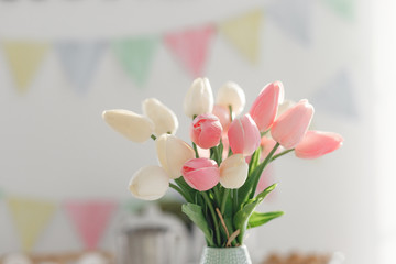 Easter home decorations, multi-colored flags, tulips and eggs on a white table on a bright clear day in a snow-white kitchen