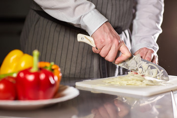 Closeup of hand with knife cutting fresh vegetable. Young chef cutting beet on a white cutting board closeup. Cooking in a restaurant kitchen