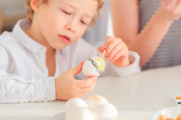 Obraz na płótnie Canvas happy young dark-haired mom and her curly blond son paint eggs for easter in the white kitchen in the Scandinavian style