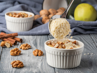 Pouring crumb topping into a cocotte bowl to make an apple dessert.