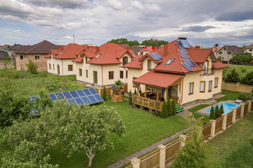 Fototapeta na wymiar Aerial view of a new autonomous house with solar panels and water heating radiators on the roof and green yard with blue swimming pool.
