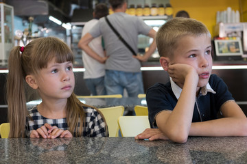 Children sitting in fast food restaurant behind empty table waiting for food.